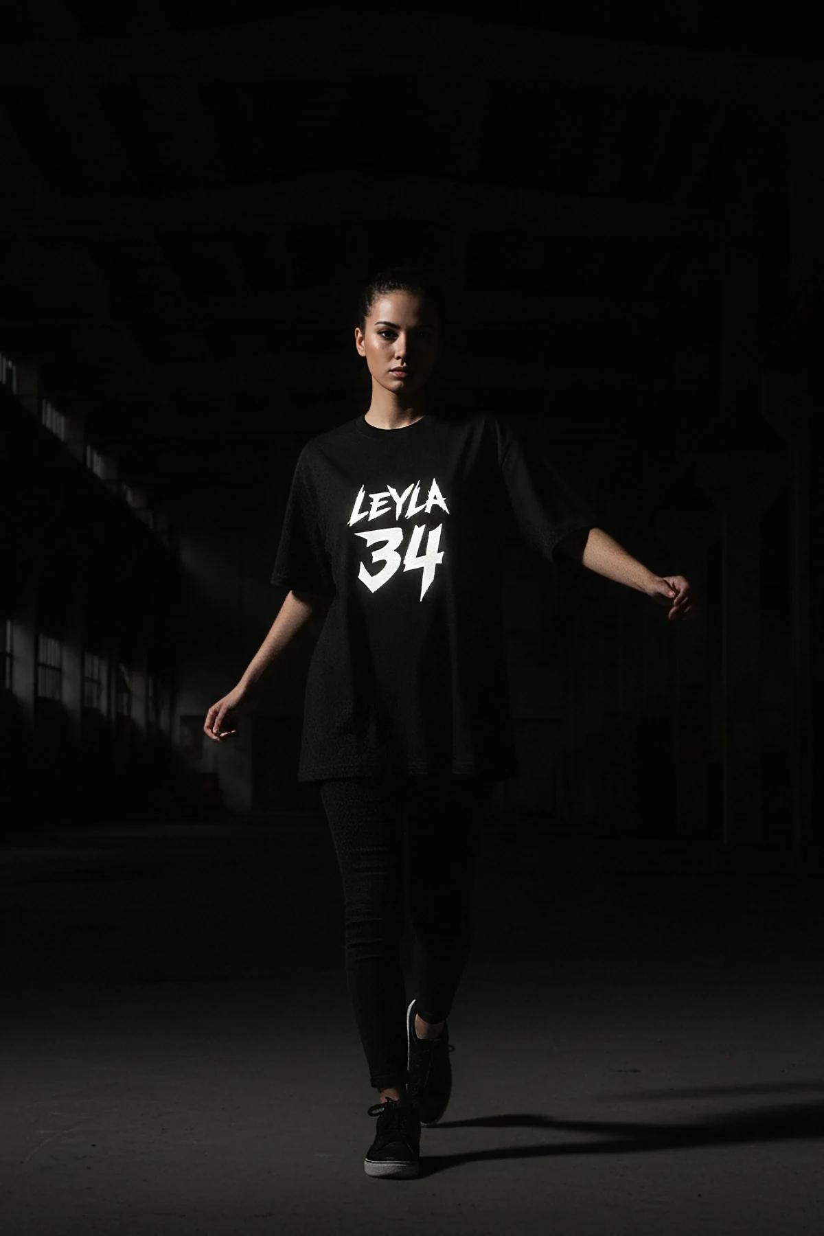 Koyu dar pantolon ile giyilen, kalın beyaz grunge grafik baskılı, box kesim ve düşük omuzlu oversize siyah pamuklu tişört