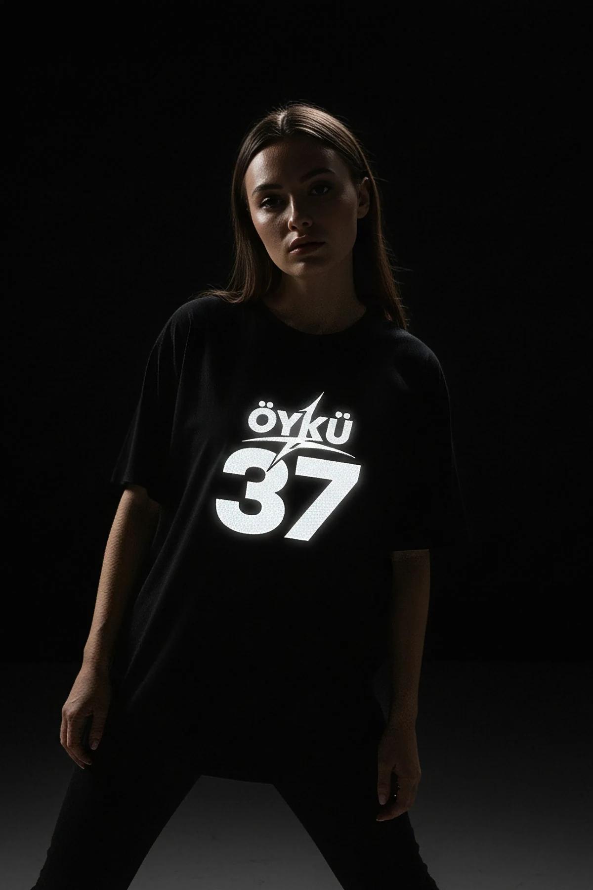 Düşük ışıkta fotoğraflanan, göğüste reflektör beyaz isim ve numara baskılı siyah oversize özel grafik tişört