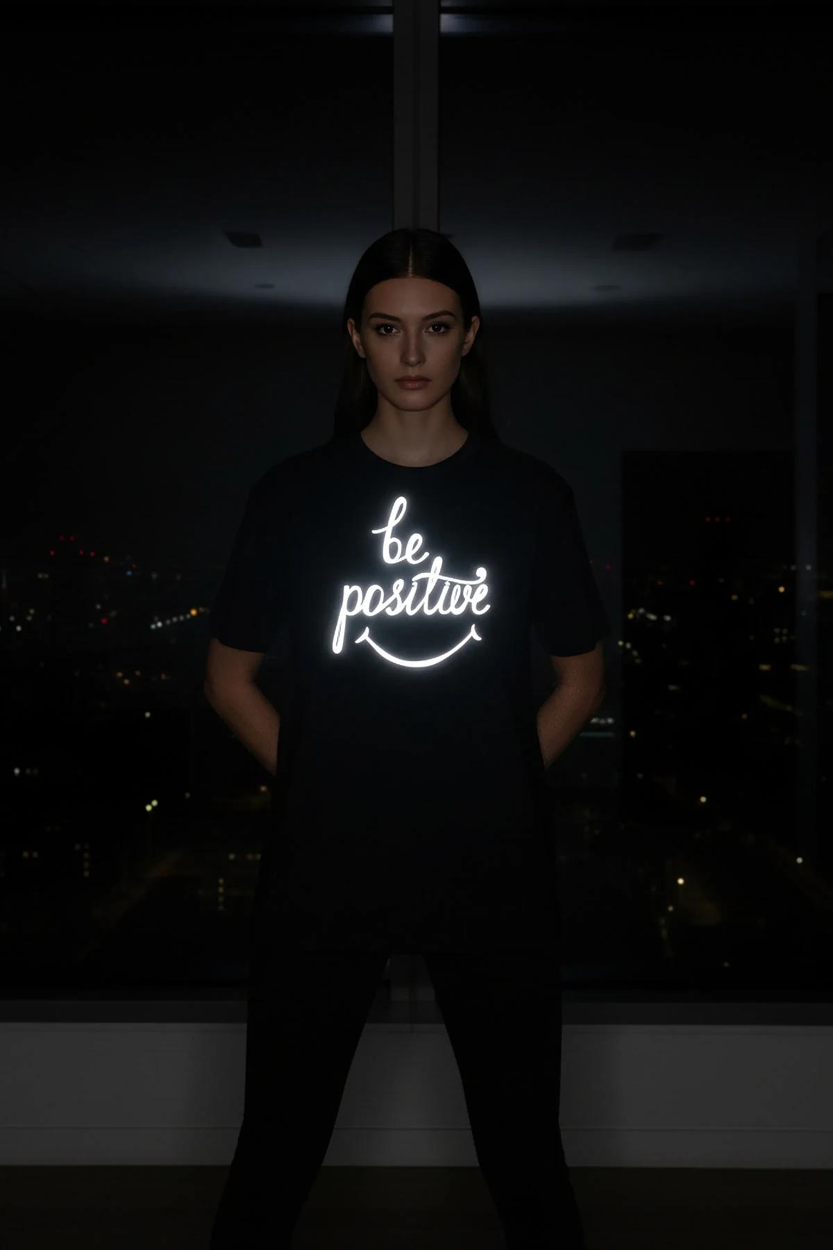 Gece giyilen, göğüste parlayan 'be positive' el yazısı ve gülen yüz baskılı reflektör oversize siyah tişört