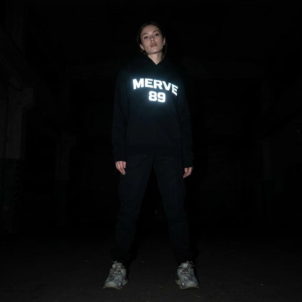 Az ışıkta siyah hoodie göğsündeki reflektör MERVE 89 blok harf baskısının yakın çekimi