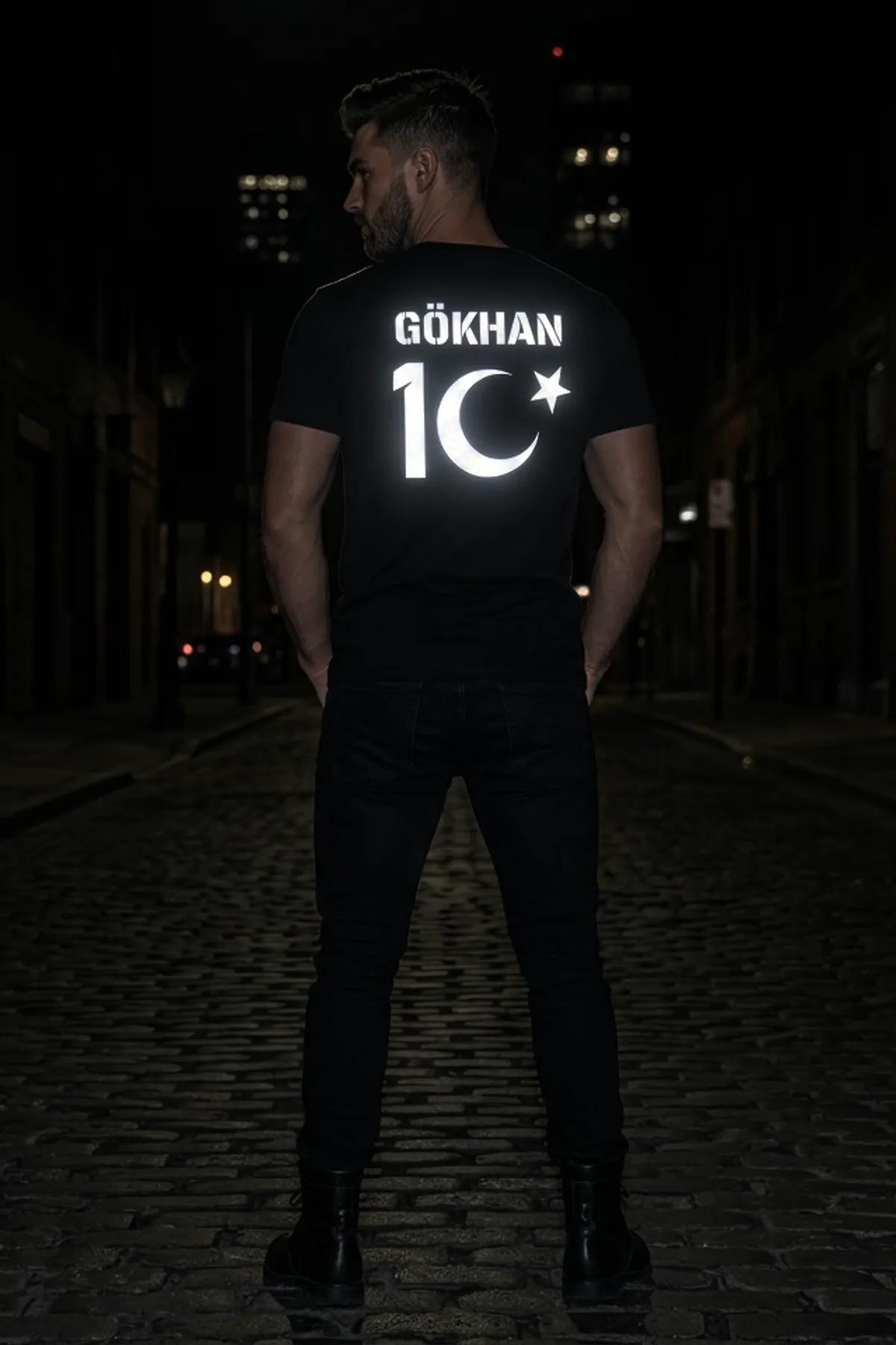 Black mens reflective t-shirt with silver-white GÖKHAN 10 crescent and star back print worn on a night street