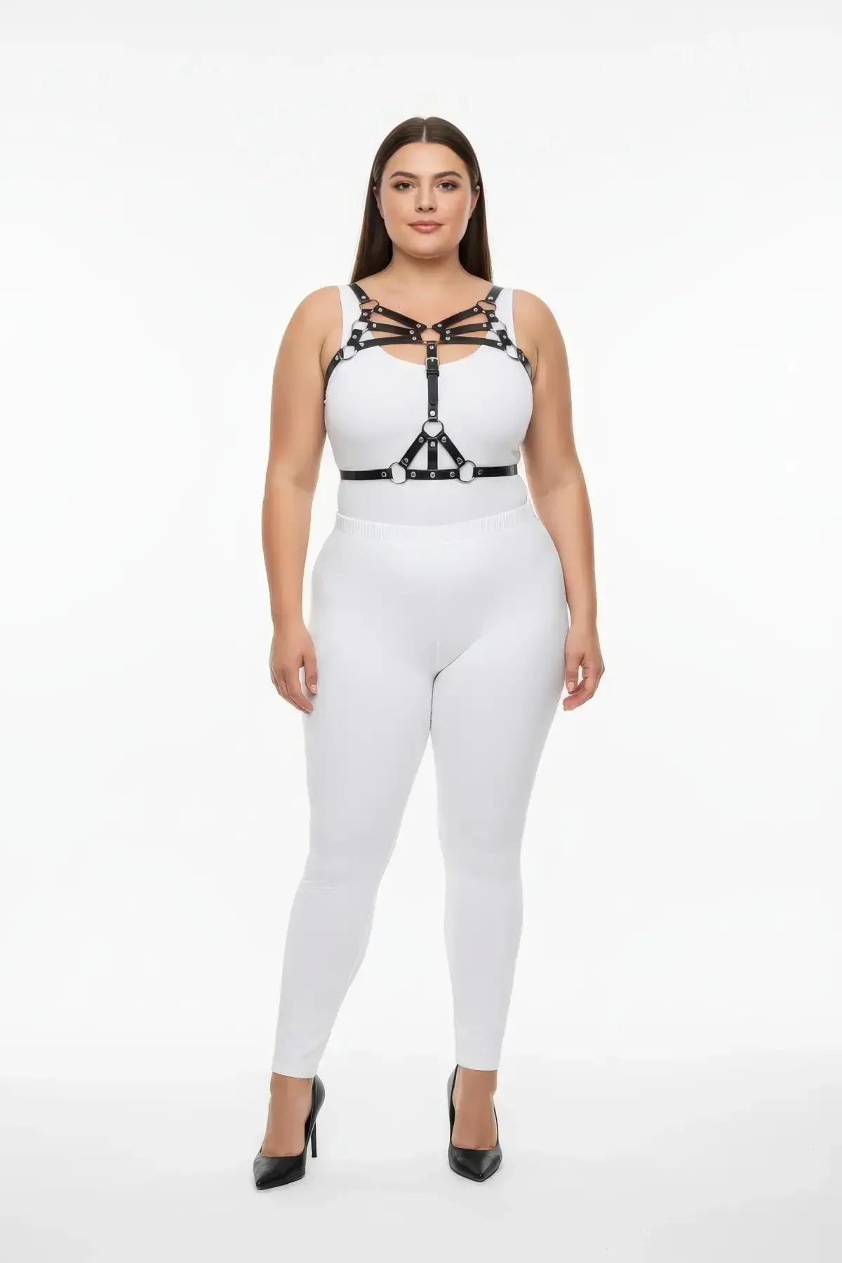 Gümüş O-halka donanımlı siyah suni deri askılı göğüs harness, beyaz crop top üzerinde katmanlı, büyük beden model