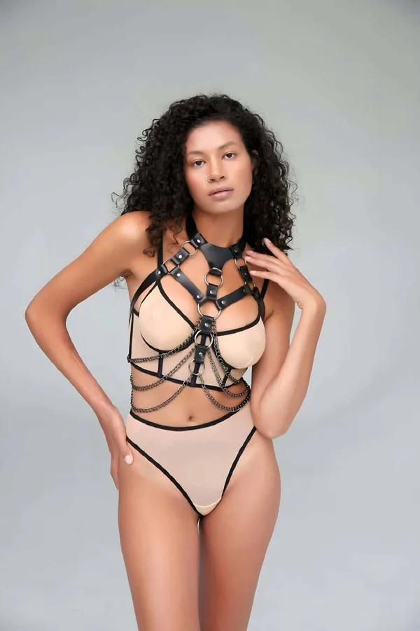 ten rengi bodysuit üzerine giyilen siyah suni deri göğüs harness, dökümlü gümüş zincirler ve dört O-halka