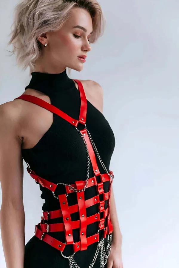 kırmızı suni deri askılı vücut harness, kafes-ızgara bel paneli, gümüş O-halkalar ve sallanan zincir detayı, siyah boğazlı kazak üzerine giyilmiş