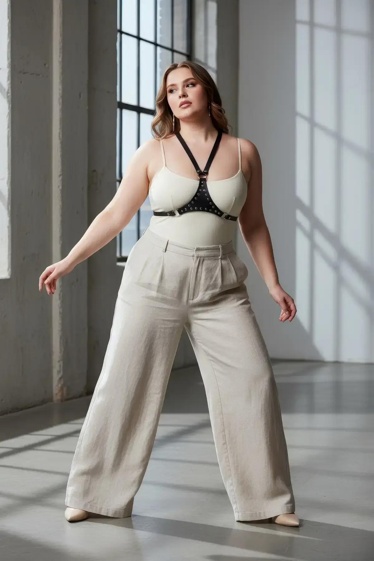 Krem bodysuit üzerinde gümüş delikli bantlı ve ayarlanabilir omuz askılı siyah suni deri zımbalı göğüs harness