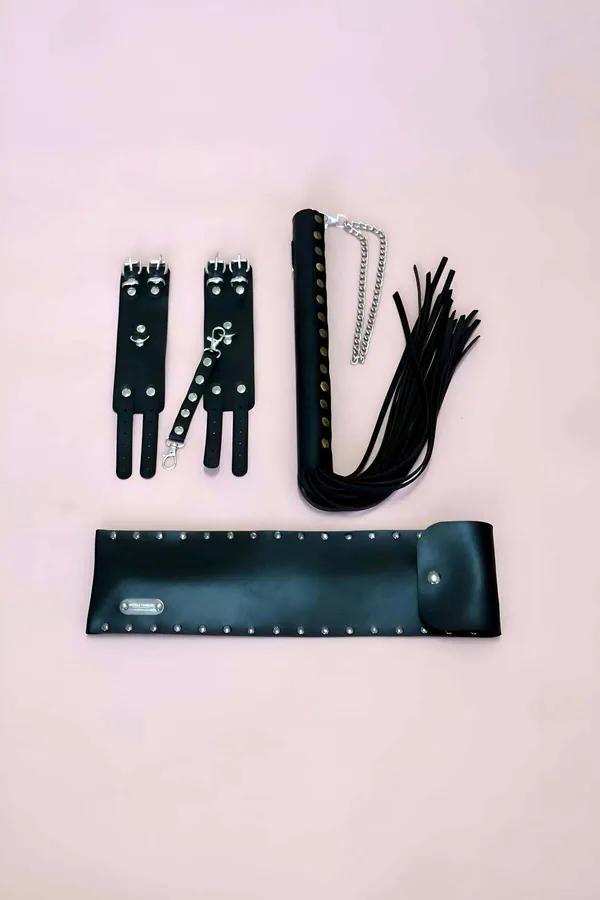 Pembe arka fonda zımbalamalı bilek kelepçeleri, gümüş zincirli flogger ve geniş zımbalamalı kemer ile siyah vegan deri 3 parça aksesuar seti