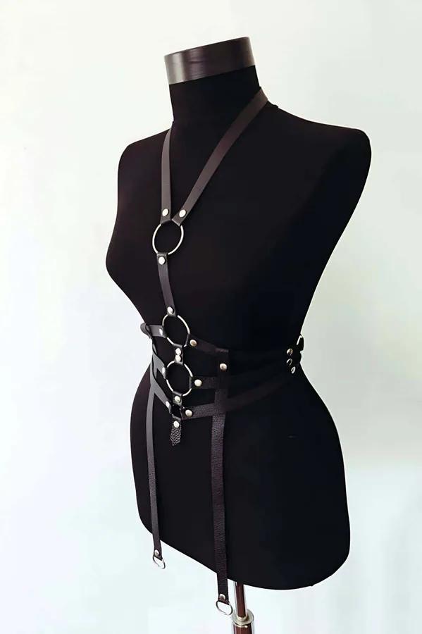 Modelde üç üst üste gümüş O-halkalar, tek omuz askısı ve çift kalça düşme bantlarıyla siyah suni deri erkek vücut harness