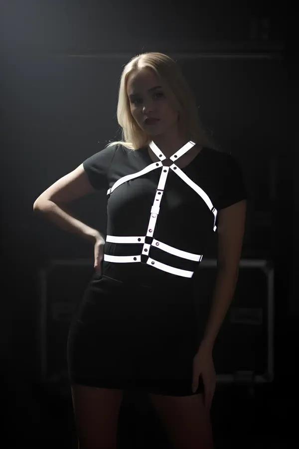Siyah kıyafet üzerine giyilmiş X-çapraz askı tasarımı ve krom çıtçıt donanımlı beyaz reflektör göğüs harness