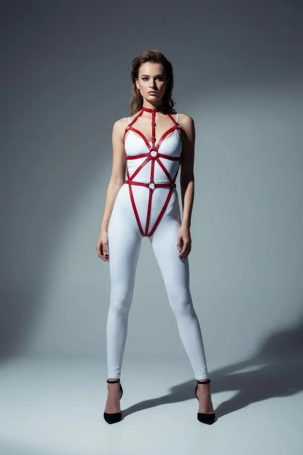 Kırmızı suni deri tam vücut harness, yayılan geometrik askılar ve gümüş O-halka detayı, beyaz body üzerinde