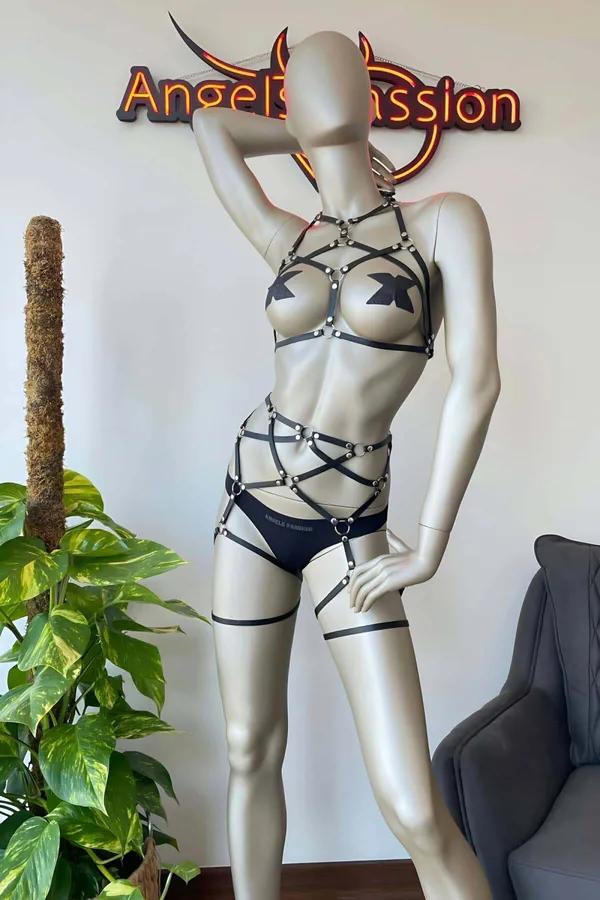 Manken üzerinde gümüş O-halkalar, çapraz askılı bel kafesi, külot ve uyluk jartiyerli siyah suni deri çok askılı tam vücut harness