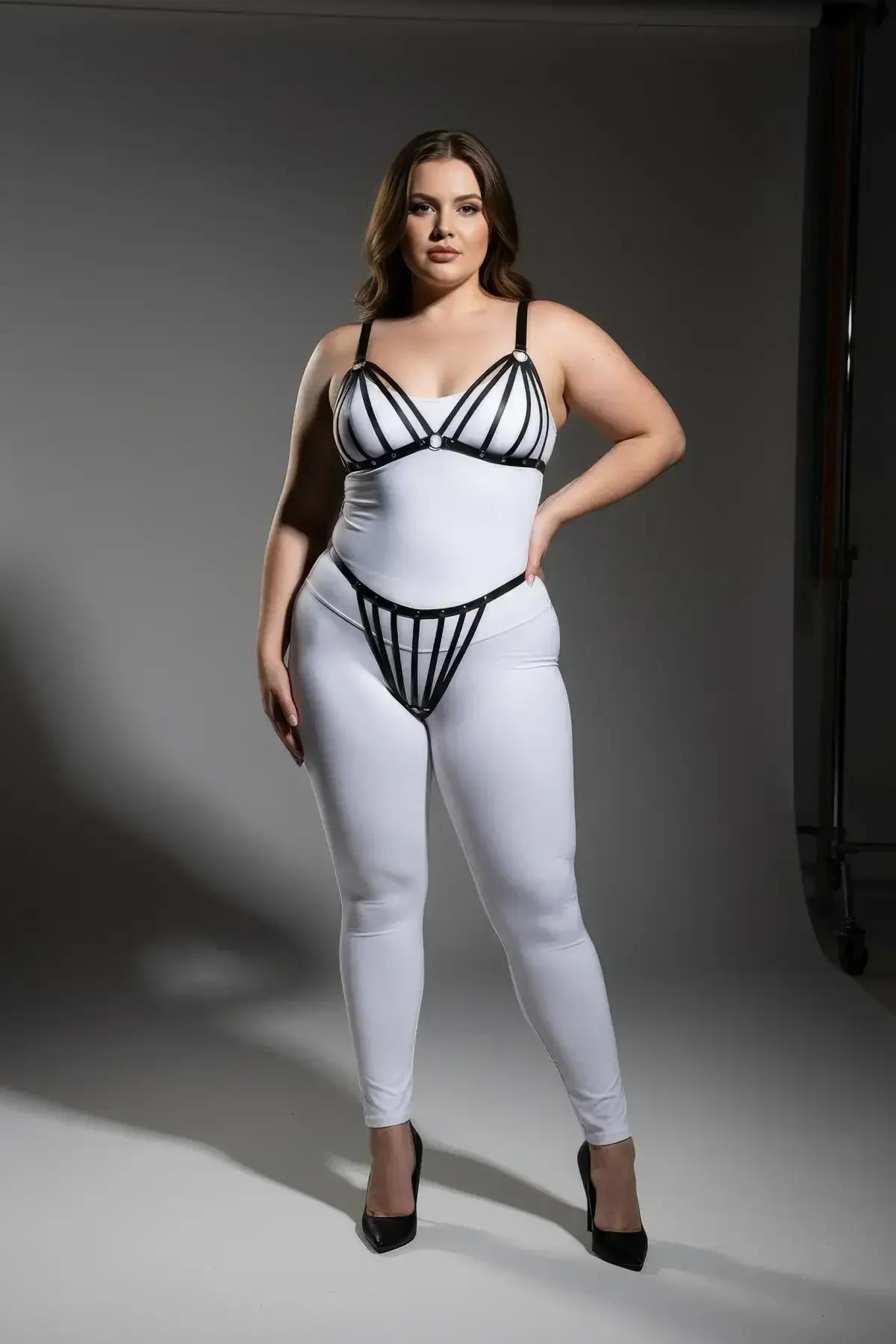 Beyaz dar bodysuit üzerinde tam göğüs kafes bant desenini gösteren siyah bantlı harness sütyen üst katman