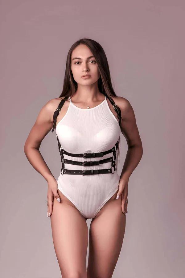 Beyaz fitilli bodysuit üzerinde giyilen altın tonlu tokalar ve D-halkalı siyah suni deri 3 askılı vücut harness