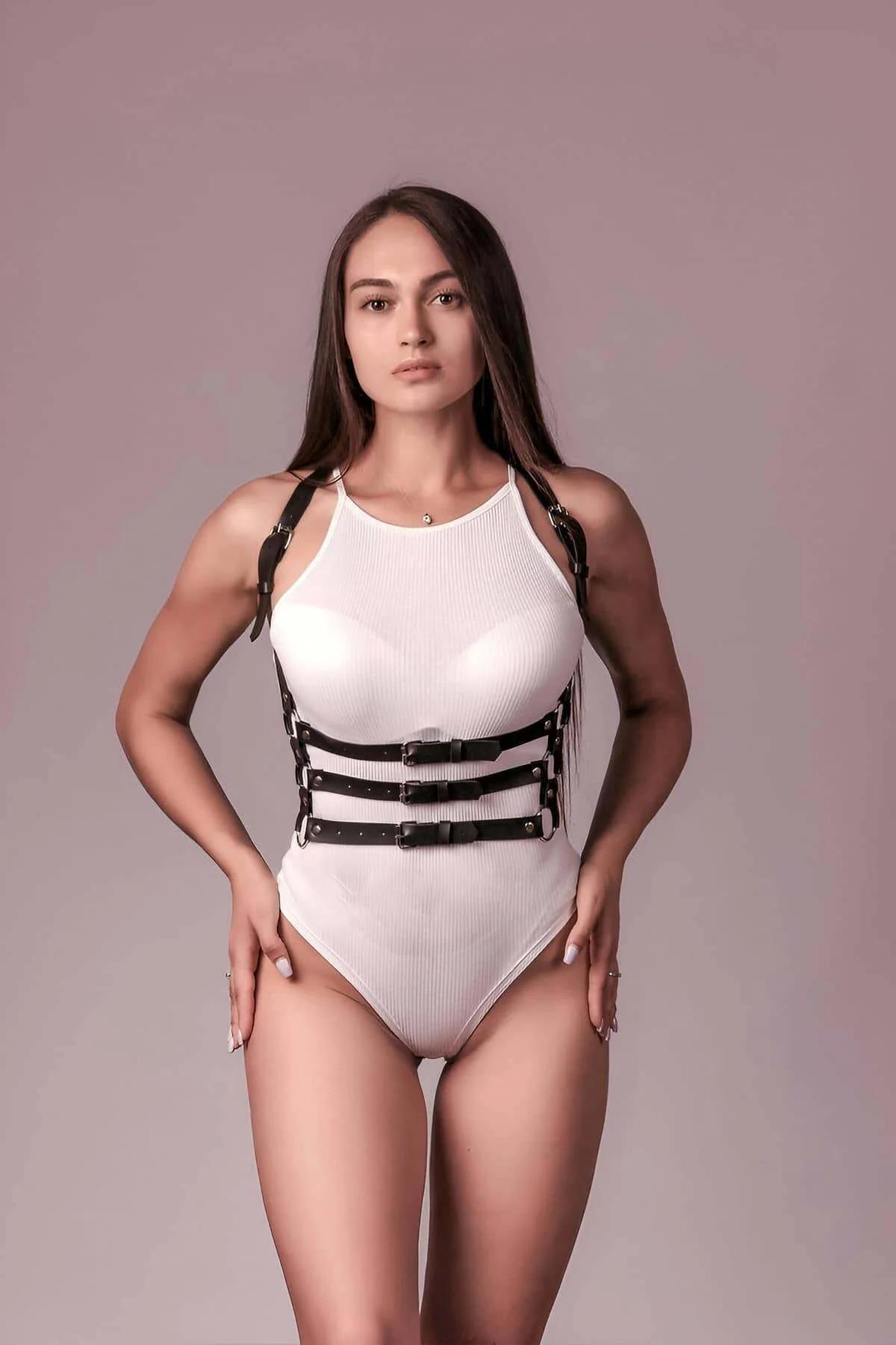 Beyaz fitilli bodysuit üzerinde giyilen altın tonlu tokalar ve D-halkalı siyah suni deri 3 askılı vücut harness