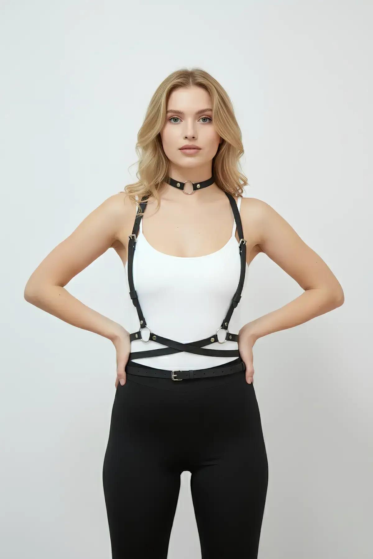 Beyaz bodysuit üzerine giyilmiş, O-halka çoker seti, altın renkli donanım ve çapraz ön bel askılarıyla siyah suni deri vücut harness