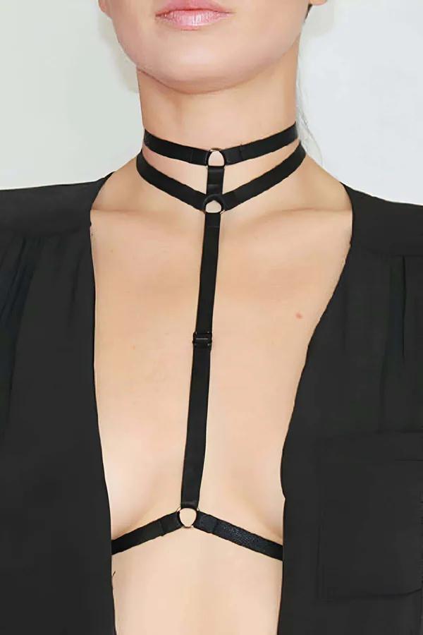 Açık siyah blazer üzerine giyilmiş altın O-halka donanımı ve dikey merkezi bantlı siyah çift askı çoker vücut harness