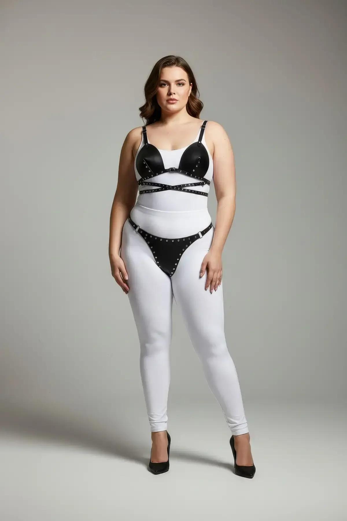 Beyaz tayt üzerinde modellenen gümüş zımba süslemeli siyah suni deri zımbalı sütyen üst ve tanga harness takımı