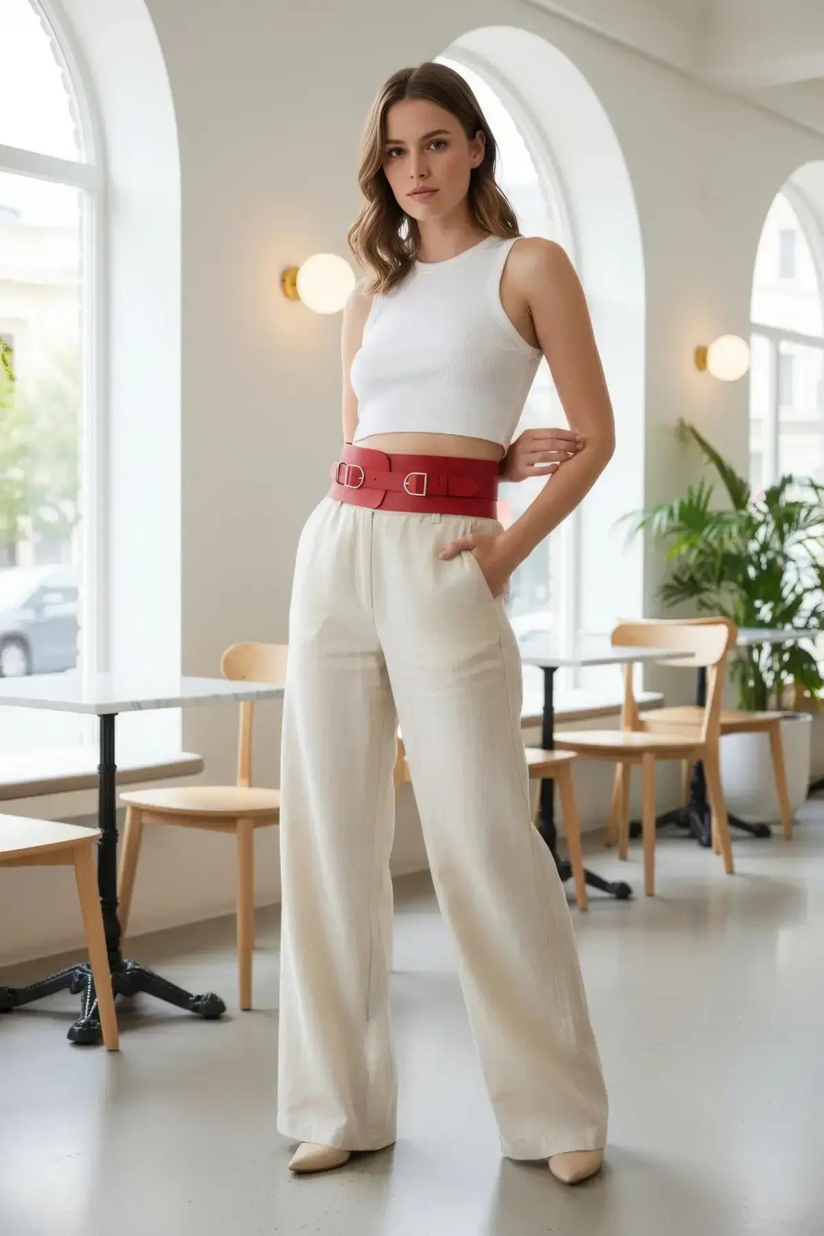 Kırmızı suni deri geniş bel sıkıştırma harness, iki gümüş dikdörtgen toka, beyaz crop top ve krem pantolon üzerinde