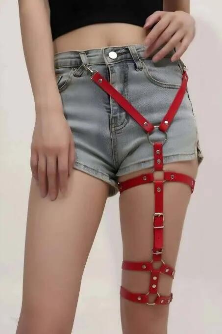Denim şort üzerine giyilen gümüş O-halka ve dört ayarlanabilir toka bant şeridi ile kırmızı suni deri uyluk harness