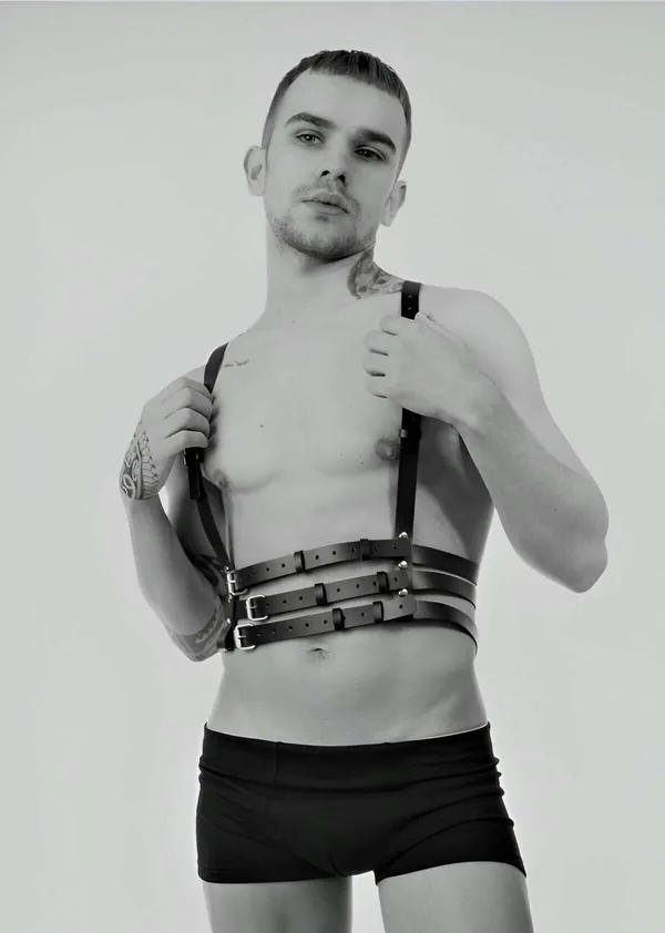 Erkek model tarafından giyilmiş gümüş dikdörtgen tokalı siyah suni deri üçlü bantlı göğüs harness ön görünüm