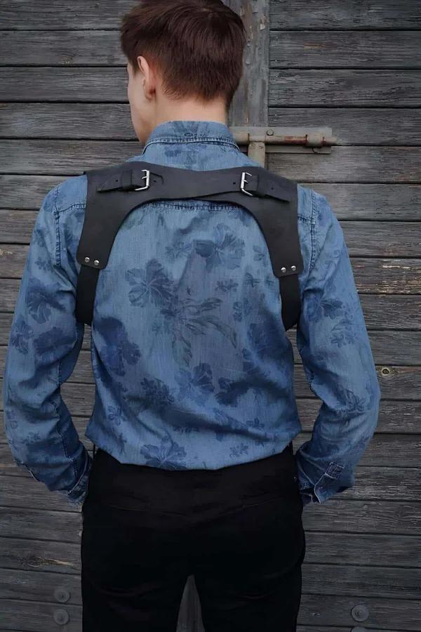 Erkek modelde çapraz X-askılı ve gümüş tonlu çift çubuklu tokalı siyah suni deri omuz harness, arka görünüm