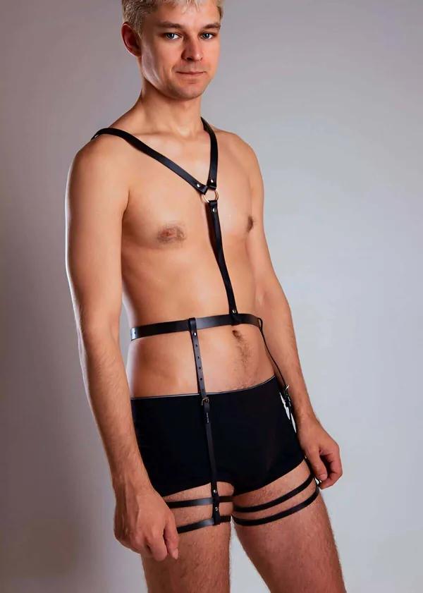 Erkek model tarafından giyilmiş göğüs kemiğinde altın O-halka, geniş bel bandı ve çift uyluk bantlarıyla siyah suni deri tam vücut harness