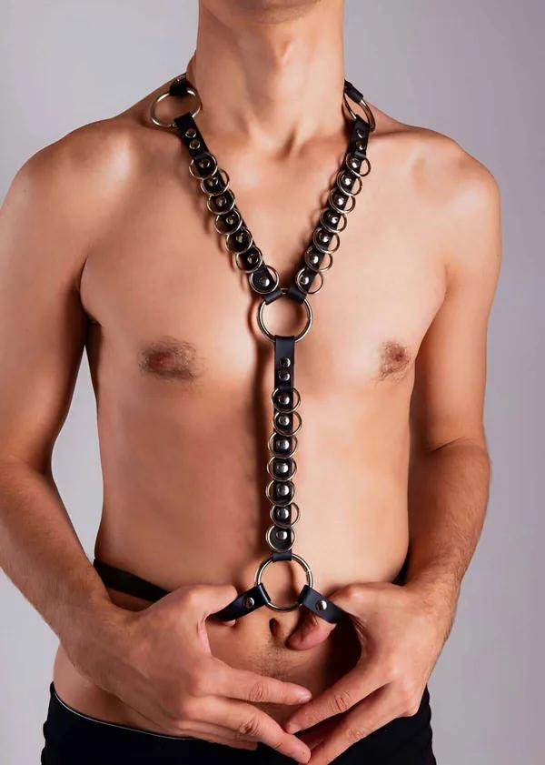 Erkek model tarafından giyilmiş boyunluktan bele uzanan kesintisiz gümüş O-halka zincirli siyah vegan deri göğüs harness
