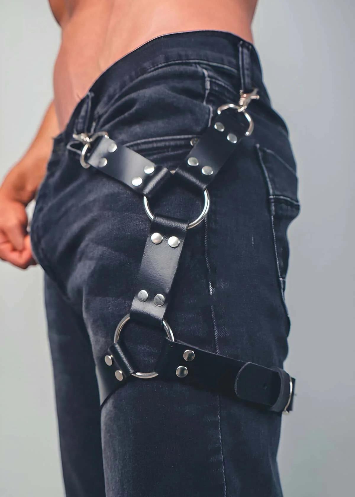 Koyu denim kot üzerinde giyilen iki gümüş O-halka ve perçin zımbalı askılarla siyah suni deri uyluk harness